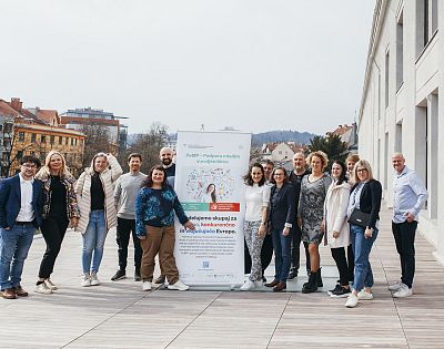 A group of people poses for a photo outdoors beside an advertising poster.