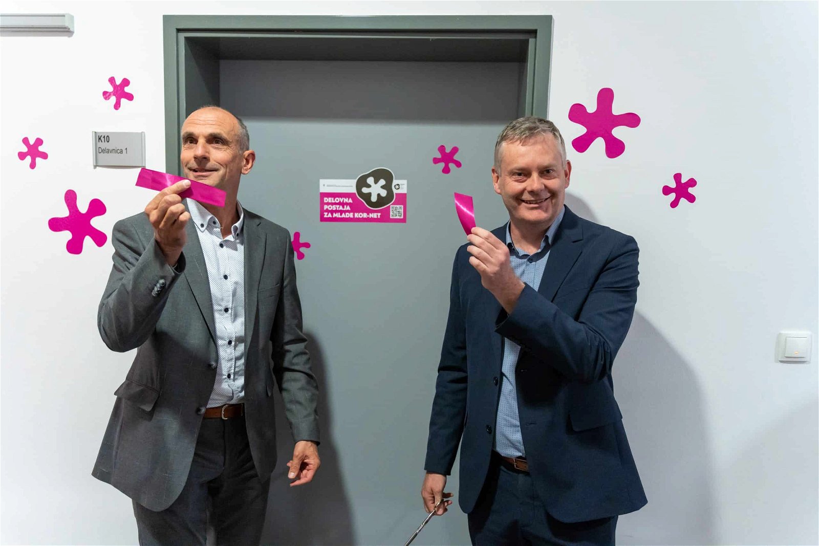 two smiling men holding the ribbon they cut earlier at the opening of the youth room