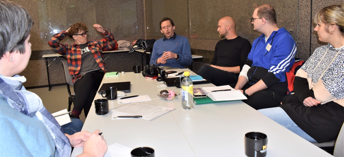 Six people gathered around a table with papers and cups. 