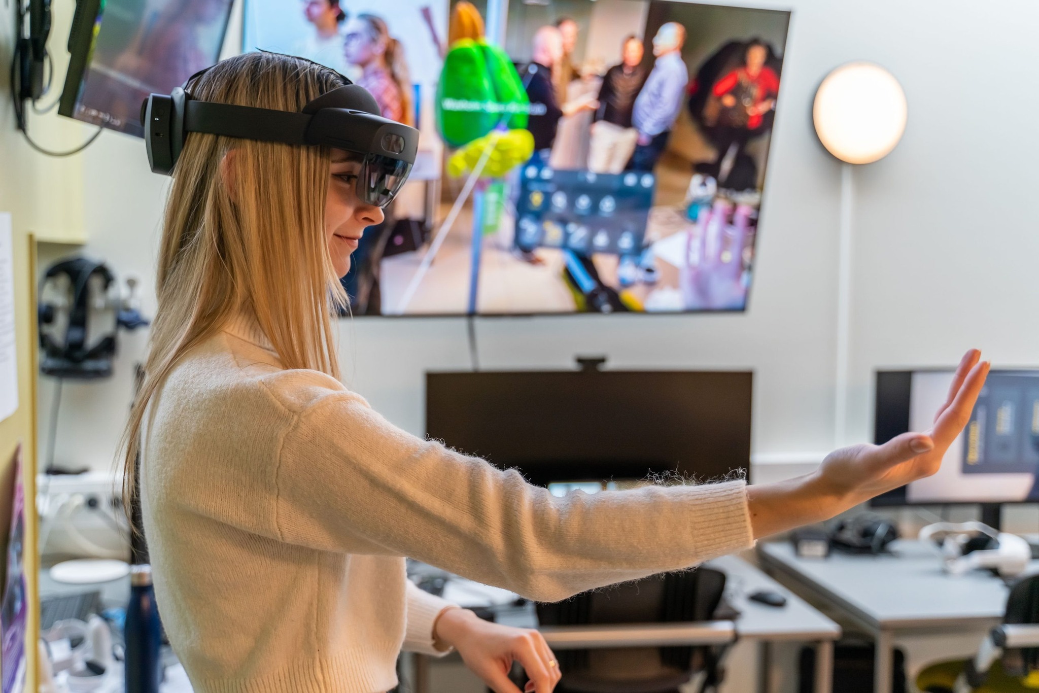 A girl with special glasses looks at her hand in front of her, screens behind