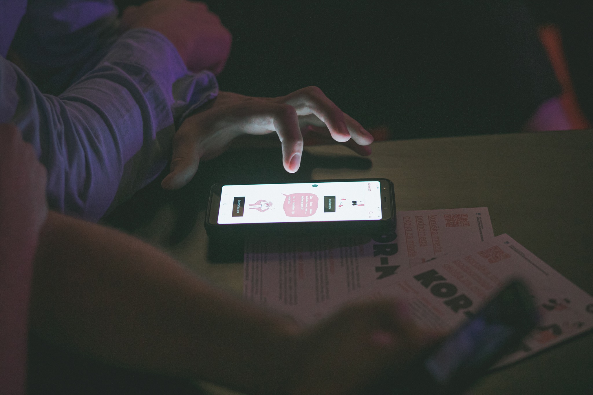 Mobile phone on the table with the website of the Koroška Virtual Youth Incubator. There are two leaflets on the table.