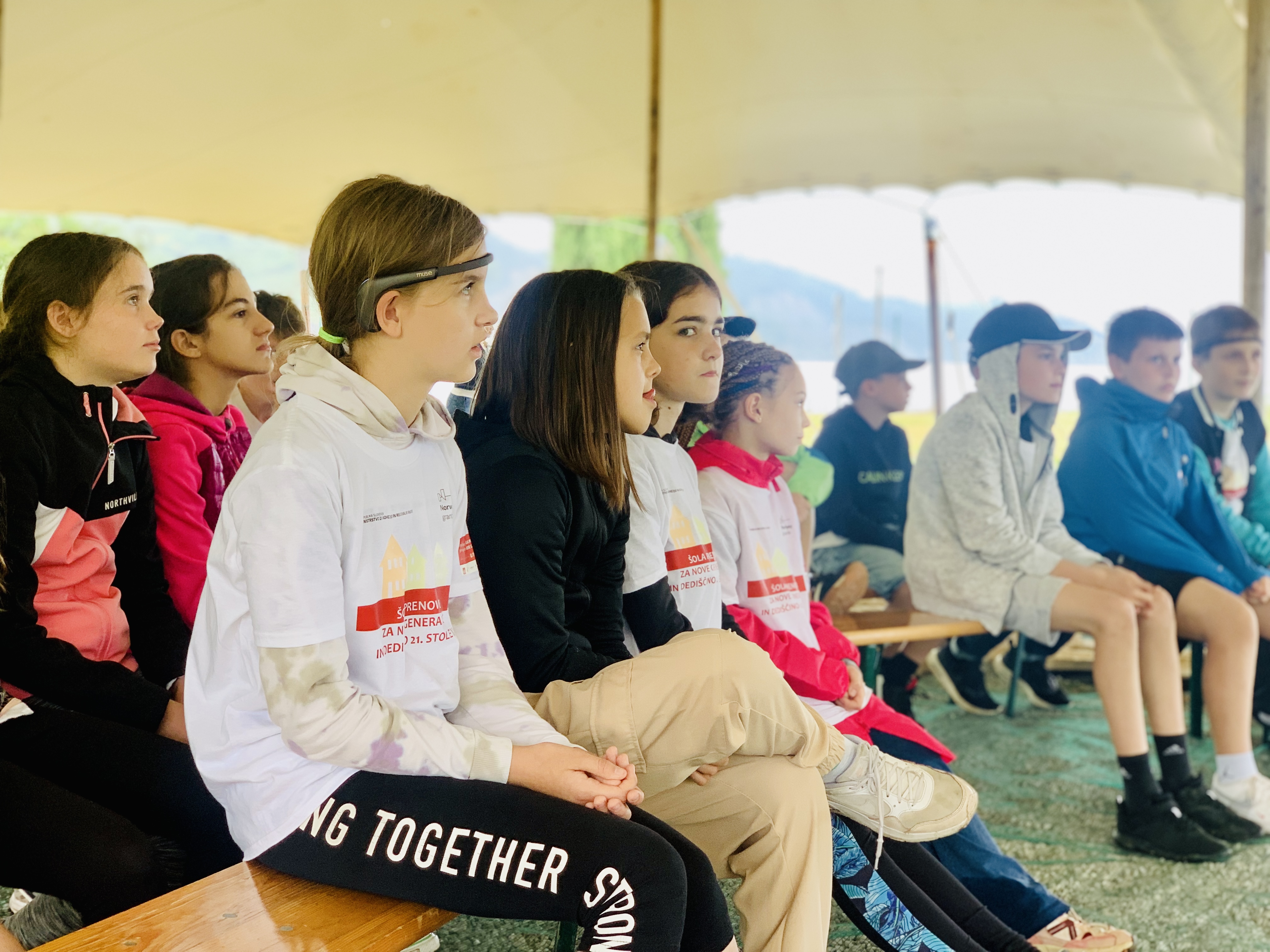 A group of students sitting on benches under a tent