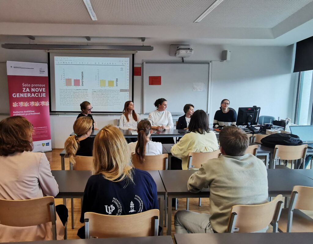 A group of people in a classroom, a presentation on a projector, a project billboard next to it, five people facing the audience.