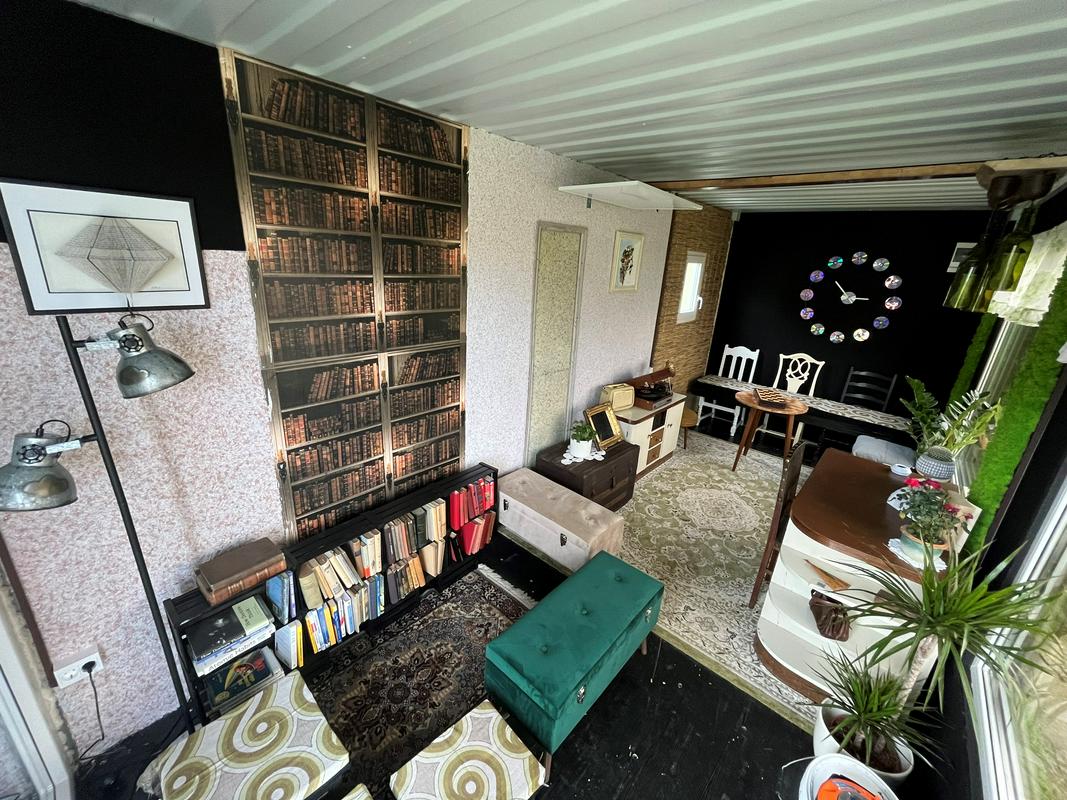 Interior of a shipping container, bookshelf, mare, chairs, clock made of CDs.