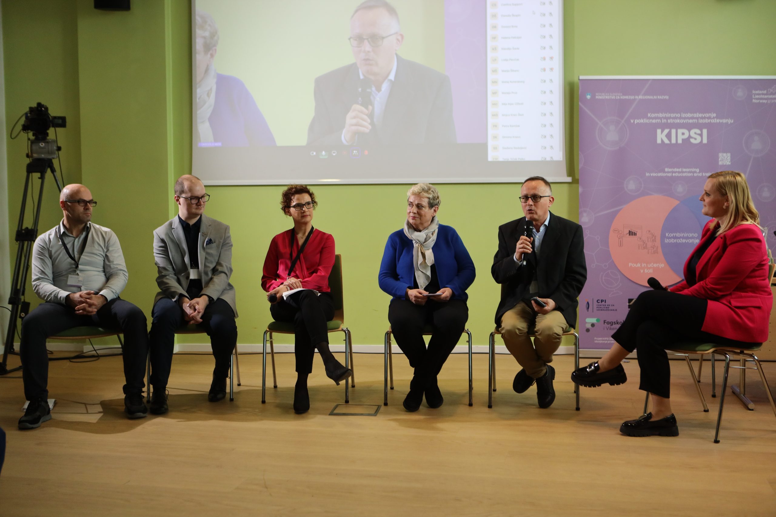 V ospredju sedijo udeleženci okrogle mize. Z leve proti desni si sledijo: dr. Mitja Veber iz Šolskega centra Novo mesto, dr. Uroš Ocepek s Srednje tehniške in poklicne šole Trbovlje, doc. dr. Danijela Makovec Radovan s Filozofske fakultete UL, dr. Slavica Černoša, vodja Sektorja za srednje šolstvo Ministrstva za vzgojo in izobraževanje (MVI), Darko Mali s Centra RS za poklicno izobraževanje in moderatorka. V ozadju se nahaja zaslon, ki prikazuje govorca, ki trenutno govori.