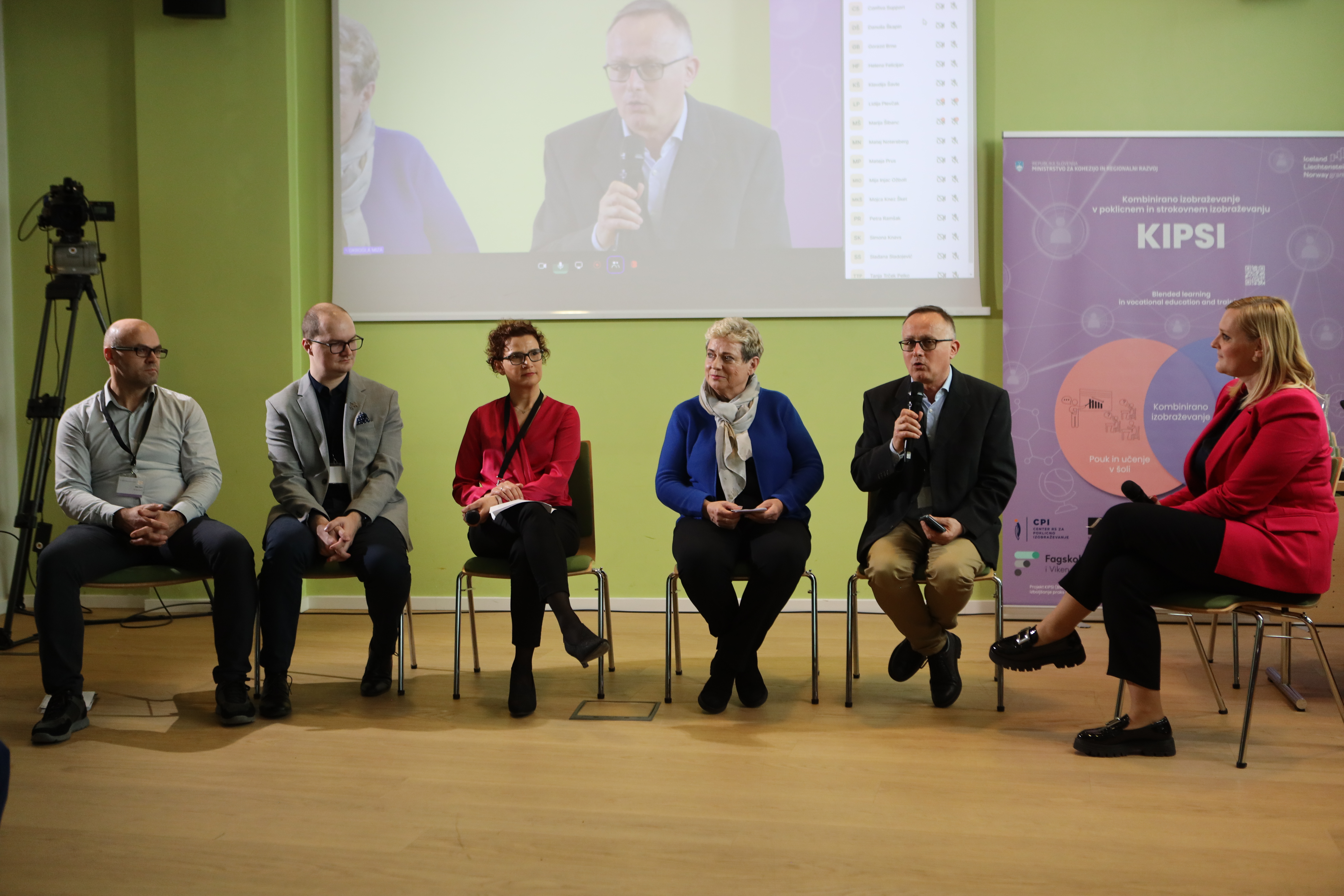 The panellists are seated in the foreground. In the background there is a screen showing the speaker who is currently speaking.