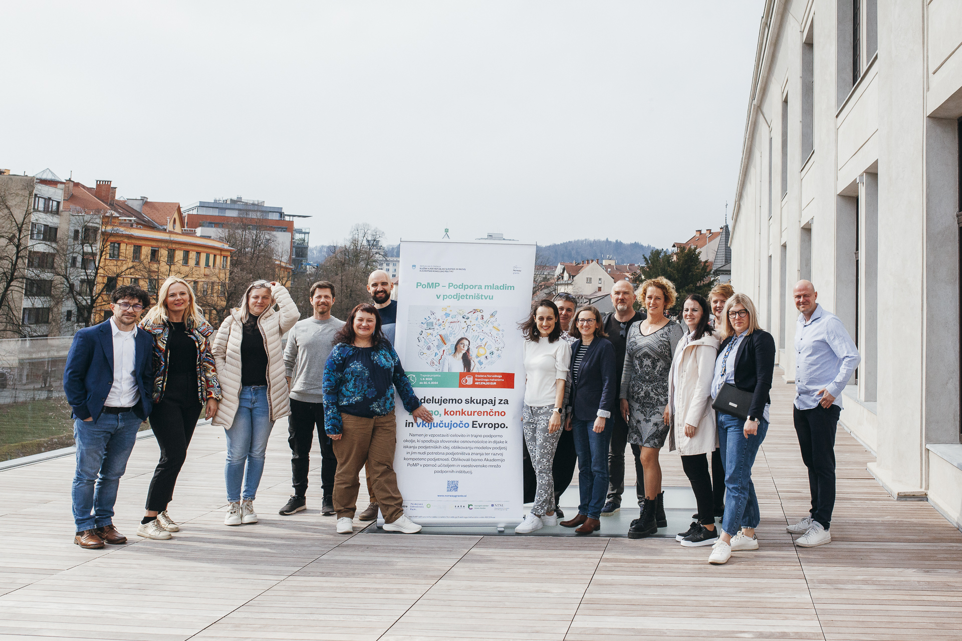 A group of people poses for a photo outdoors beside an advertising poster.