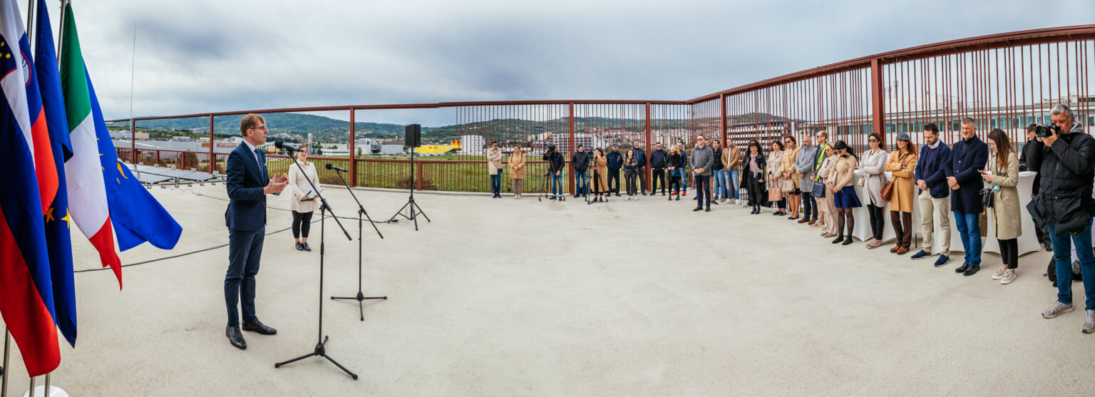 Event venue. There is a person at a standing microphone who is giving a speech. Participants stand in the background.