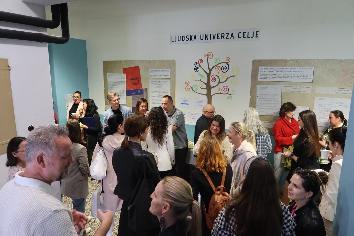 A crowd of people gather for food and drinks in the corridor of a school.