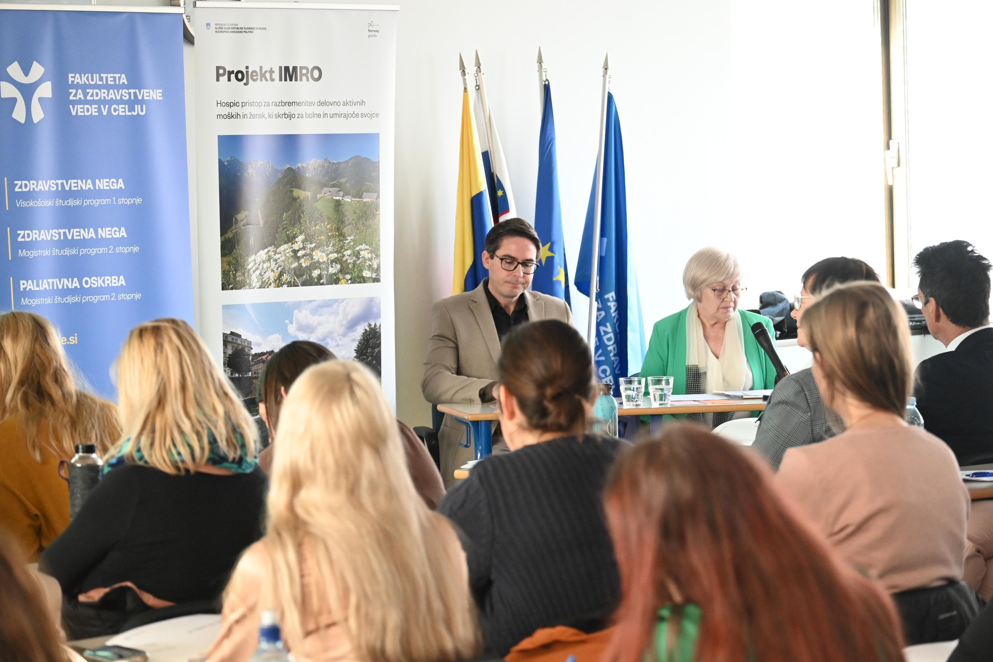 Udeleženci konference sedijo na stolih in spremljajo potek konference. V ospredju sedijo predstavniki Mestne občine Koper in Slovenskega društva Hospic.